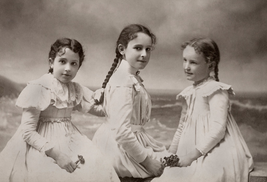 The three Johnston sisters as girls — studio portrait with a painted seaside backdrop, est. late 1890s. Edith is one of the three (with Kathleen and Mary).